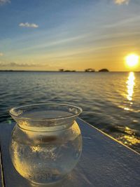 Close-up of drink against sea at sunset