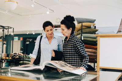 Woman assisting customer choosing wallpaper sample in store