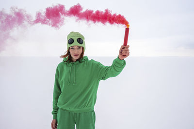 Woman holding red smoke distress flare against sky