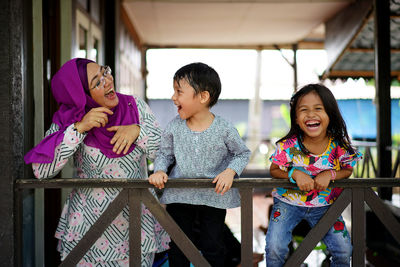 Portrait of smiling mother and children standing against railing