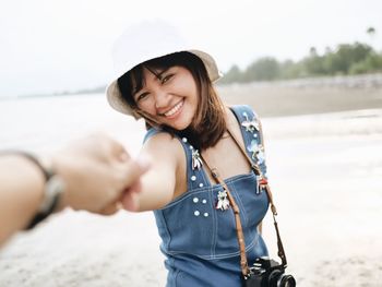 Cropped hand holding cheerful young woman at beach