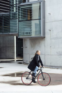 Woman doing cycling on road by building