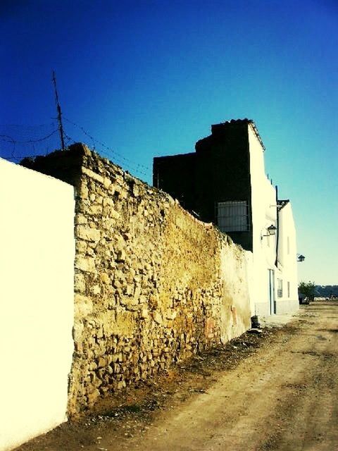 architecture, built structure, building exterior, clear sky, blue, copy space, house, wall - building feature, sunlight, street, the way forward, road, residential structure, building, day, outdoors, low angle view, old, no people, wall