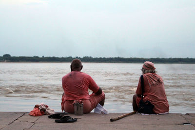 Rear view of men sitting on beach against sky