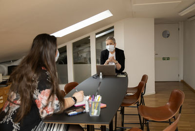 Female coworkers with protective face masks talking in office