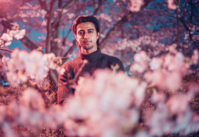 Portrait of confident young man standing by cherry tree at night