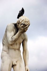 Low angle view of pigeon perching on statue against cloudy sky