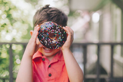 Portrait of boy holding chocolate donut while standing outdoors