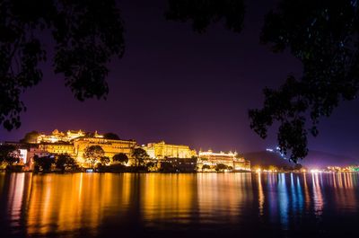 Illuminated buildings by river against sky at night