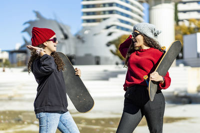 Happy female friends holding skateboards while high-fiving in city