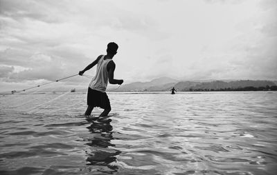 Rear view of man standing in sea against sky