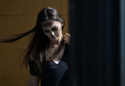 Woman with spooky halloween make-up standing against wall