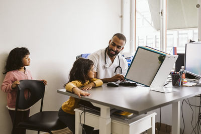 Smiling male pediatrician talking with girl sitting at desk