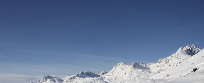 Low angle view of snowcapped mountains against clear blue sky