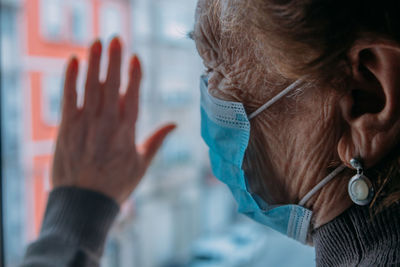 Close-up of senior woman wearing mask seen through window