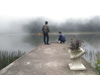 Friends on pier over lake against sky during foggy weather