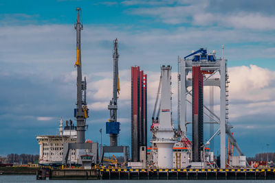 Cranes at harbor against sky