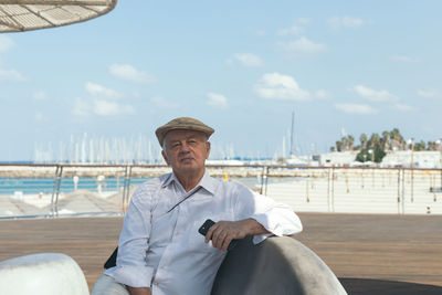 Portrait of senior man sitting on chair at harbor