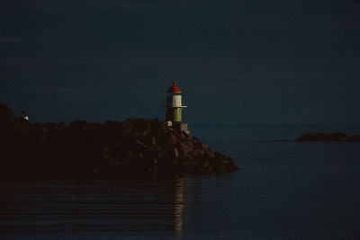 Lighthouse amidst buildings and sea against sky