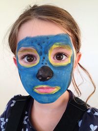 Close-up portrait of girl with painted face against wall