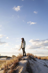 Woman with hands in pocket looking away while standing on sand dune