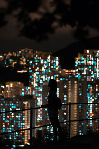 Rear view of silhouette man standing against illuminated buildings in city