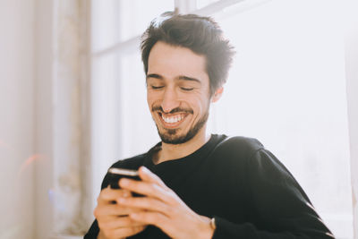 Happy young man using smart phone at home