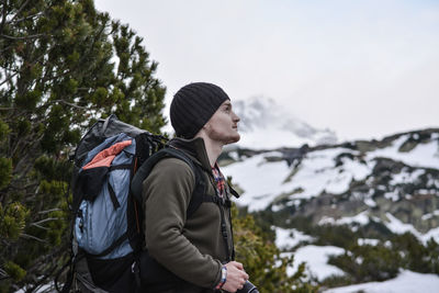 Side view of hiker with backpack while standing on snow covered mountain against sky