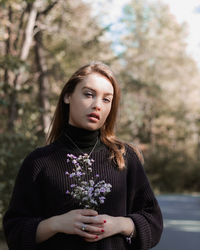 Portrait of young woman standing against trees on road