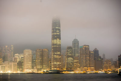 Illuminated skyscrapers at victoria harbour against sky