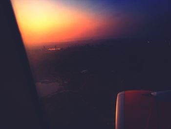 Cropped image of airplane flying over landscape against sky during sunset