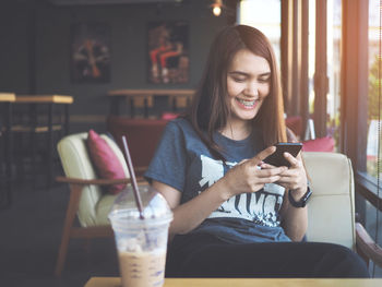 Smiling woman using mobile phone while sitting by drink on table