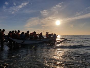 People enjoying in sea against sky during sunset