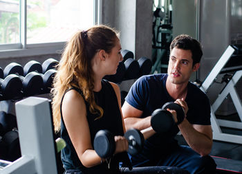 Trainer watching woman lifting dumbbell in gym
