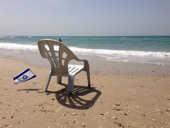 Empty chair at beach against clear sky