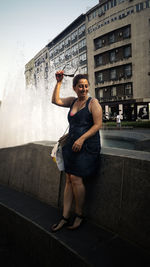 Woman with sunglasses standing by retaining wall against fountain in city