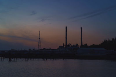 Silhouette of factory against cloudy sky during sunset