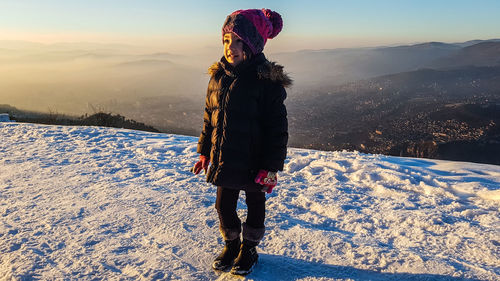 Cute girl standing on snow against sky during winter