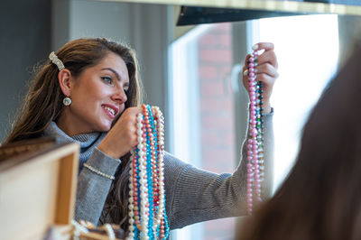 Reflection of a woman in mirror choosing and trying different jewelry, soft focus, close-up