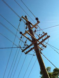 Low angle view of electricity pylon against clear blue sky