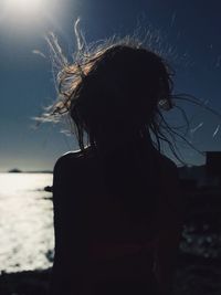 Rear view of silhouette woman with tousled hair at beach