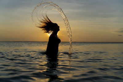 Silhouette woman by sea against sky during sunset