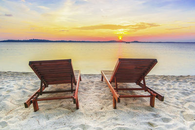 Chair on beach against sky during sunset