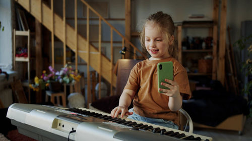 Smiling girl holding mobile and playing piano