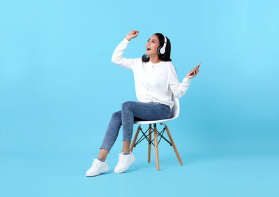 Full length of senior woman sitting on chair against blue background