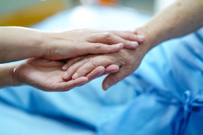 Cropped image of doctor and patient holding hands in hospital