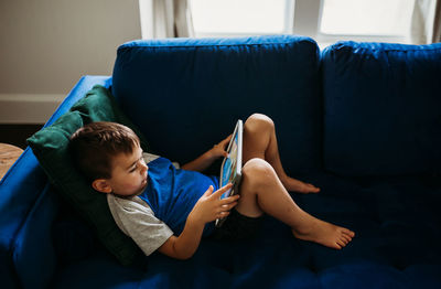 Over head view of young boy laying on couch with tablet