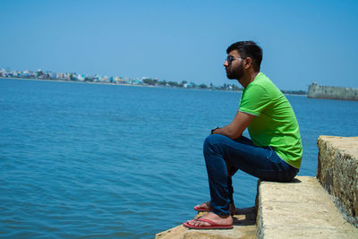 Side view of young man looking at sea against blue sky