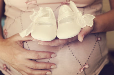 Midsection of pregnant woman holding shoes at home