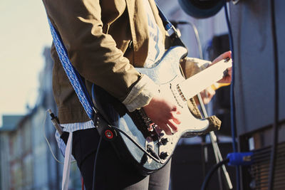 Midsection of man playing guitar at concert in city